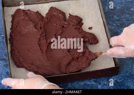 Cheese brownie dough is laid out in a metal mold. The process of making a cheese brownie. Blue marble background. Close-up. Stock Photo