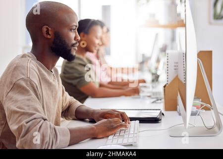 The pressure is on and were ready for it. Shot of a businessman working on his computer while his colleagues sit in the background. Stock Photo