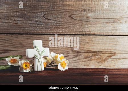 Easter holiday conceptual background on rustic wooden boards. Photo of gingerbread cookie Cross shape, narcissus or daffodils flowers on table top. Card with copy space to place text. Minimal concept Stock Photo