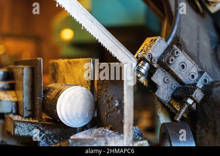 A metal band saw in the workshop cuts a metal rod with a liquid refrigerant. Gear blade of the machine. Stock Photo