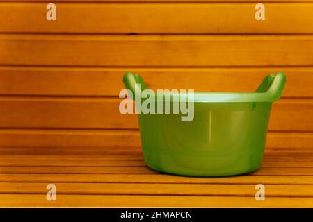 Plastic green basin on a wooden shelf in the sauna. Stock Photo