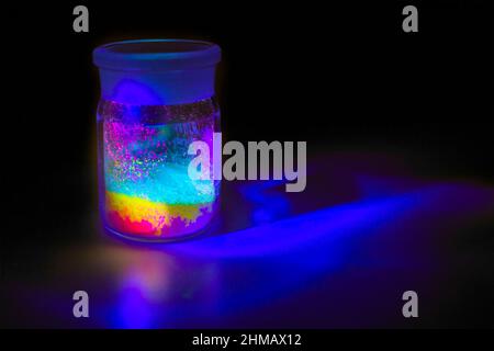 Fluorescent organic materials like a powder of red, yellow, and green color for the production of OLED inside glass bottles in UV light. Stock Photo