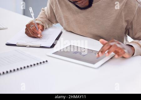 The numbers are looking good. Cropped shot of a businessman using a digital tablet while filling in some paperwork. Stock Photo