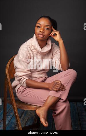 A confident young black woman sitting on a chair with one leg on another Stock Photo