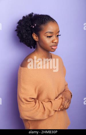A pretty young British black woman standing against a purple background and looking away Stock Photo
