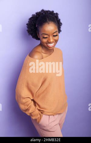 A young black woman standing near a background with her hands in her pockets. Stock Photo