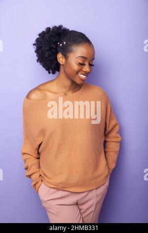 A young black woman standing near a background with her hands in her pockets. Stock Photo