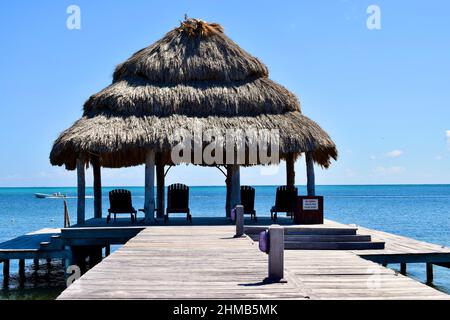 A palapa over the water at a beach hotel facing the Caribbean Sea with a small fishing boat passing in the background in San Pedro, Belize. Stock Photo