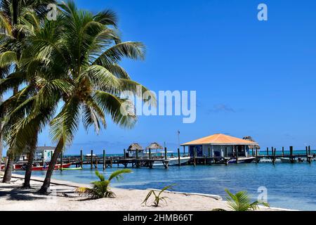 A view from the beach of some buildings over the water, boats, piers, and palm trees on San Pedro, Belize. Stock Photo