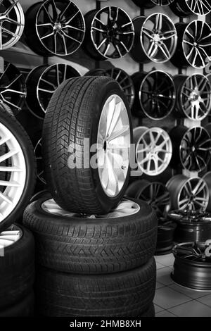 rubber car wheels lie in a pyramid against the background of car alloy wheels in a store. Sale and replacement of wheels and discs. Stock Photo