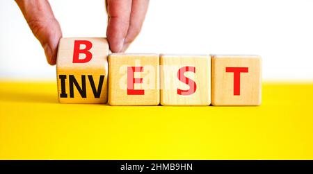 Best invest symbol. Businessman turns a wooden cube and changes the word Invest to Best. Beautiful yellow table, white background. Business and best i Stock Photo