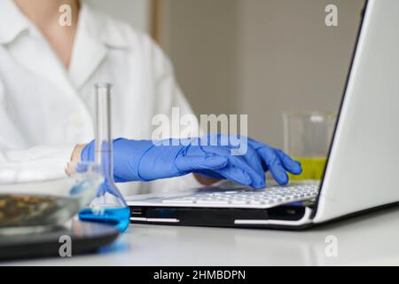 Female scientist in white coat typing on laptop computer keyboard in laboratory. Online medical working. Stock Photo