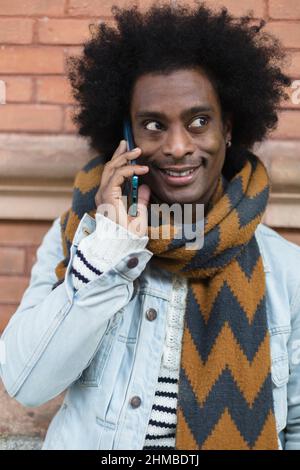 Portrait of young African American man with afro hairstyle and fashionable clothes talking on the phone outdoors. Stock Photo