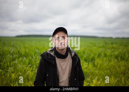 The guy is standing in a cornfield. A man in black clothes. The young man is traveling. The person is in a good mood. Overcast weather. Stock Photo