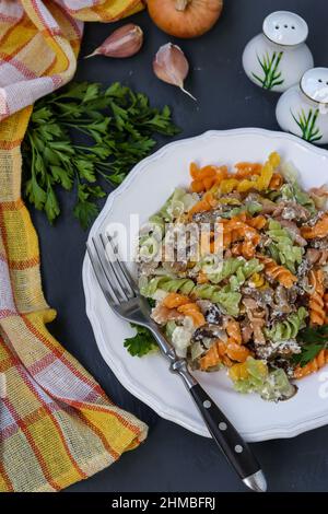 Multicolored fusilli pasta with mushrooms in a white plate on a dark background, top view Stock Photo