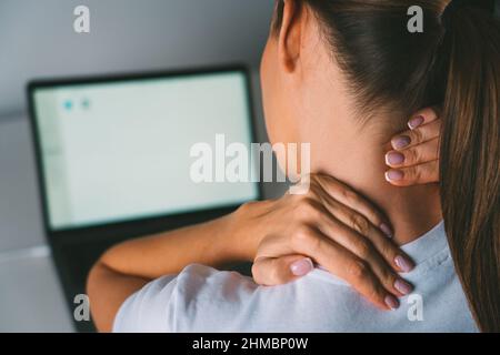 Neck pain after working on laptop or computer. Young woman massaging neck to relieve pain after working on pc Stock Photo