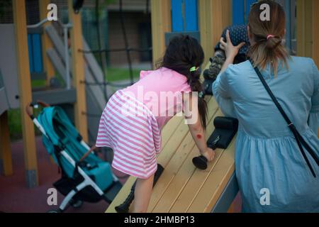 Child climbs wall. Girl plays on playground. Preschooler climbs inclined plane clinging to special ledges. Active lifestyle. Stock Photo