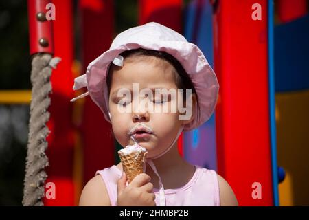 A girl eats ice cream in the playground. The child eats sweetness in the summer. Walk with a child in the playground. A preschooler in Panama. Stock Photo