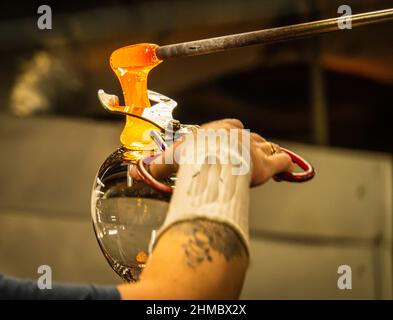 glass blowers working together to cut the molten glass to create a goblet Stock Photo