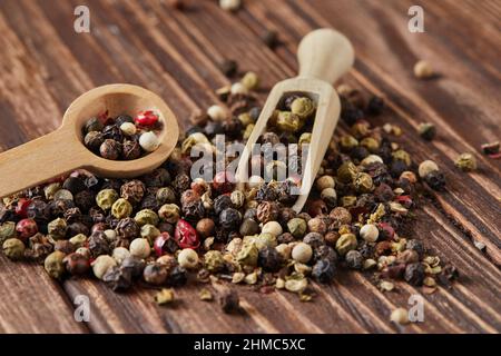 Multicolored peppercorns mix with wooden spatula and spoon is scattered over vintage wood background. Stock Photo