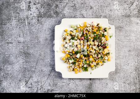 Surimi crab sticks salad with corn, cucumber and seaweed on a white square  plate on a dark background. Top view, flat lay Stock Photo