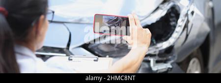 Woman insurance agent taking pictures of broken car on mobile phone closeup Stock Photo