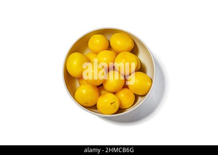 Lots of yellow plums in a white deep dish on a white background, view from above Stock Photo