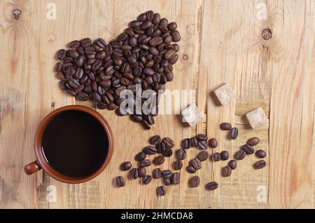 Cup of coffee, heart made from beans and sugar cubes located on old wooden background, top view Stock Photo