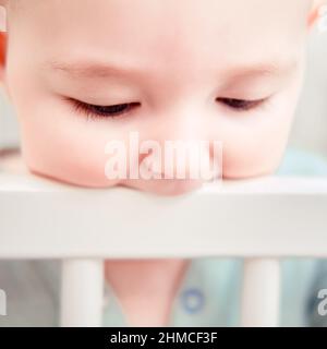 Baby gnaws at the edge crib during teething itching. Funny child scratching his teeth on the rail bed, age six months Stock Photo