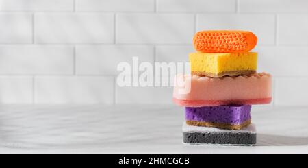 Multicolored sponges for washing dishes are stacked on a white tiled background. Stock Photo