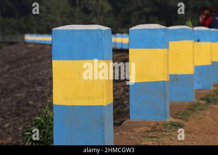concrete pivots painted in blue and yellow to delimit parking areas on the side of the dam. Road barriers for safety Stock Photo