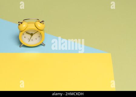 Yellow alarm clock on a yellow, blue and green background. Copy space. Time concept. Stock Photo