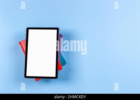 Digital tablet computer, e-book reader on top of pile of books on light blue background. Top view, copy space. Mock up Stock Photo