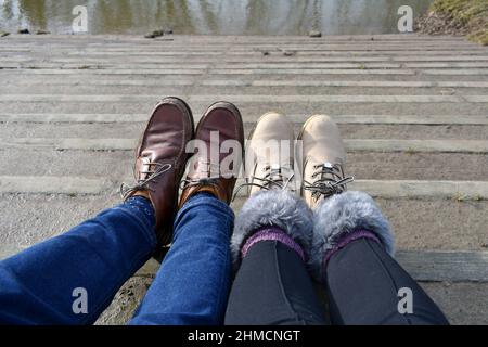 close up man and woman's feet wearing lace up walking boots on steps looking downward. People with feet up, taking a break outside in summer sunshine Stock Photo