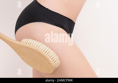 woman massaging the her leg skin with a dry massage brush. anti cellulite peeling body care. Close-up Stock Photo