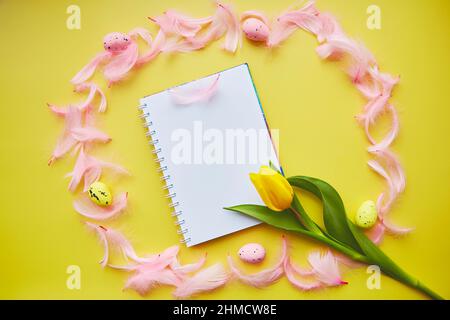 Creative Easter stationery card mock up on yellow background. Decorated Easter: colorful eggs, pink feathers and yellow tulip. Stock Photo