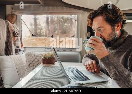 Mature man working on laptop computer inside a camper van with nature outdoors view outside the window. Concept of freedom and vanlife lifestyle. Smar Stock Photo