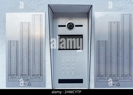 Silver and modern intercom with camera of two skyscrapers and codes by floors located on the entrance wall. Backlit digits. Stock Photo