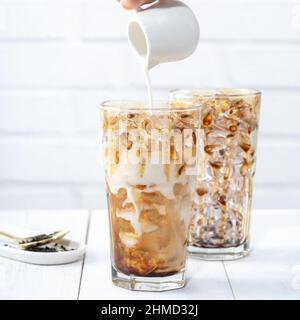 Making bubble tea, pouring milk into brown sugar pattern drinking glass cup on white wooden table background. Stock Photo