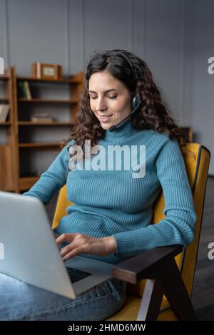 Young female freelancer using headset for remote work, communicating with colleagues via videocall Stock Photo