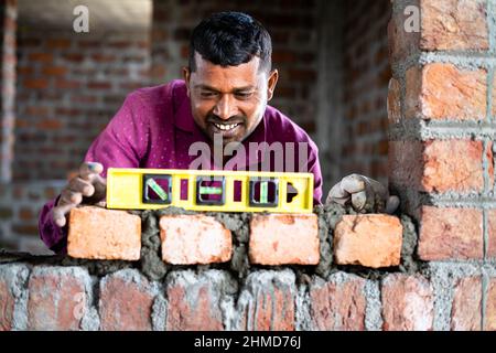 Mason measuring horizontal surface of wall using spirit level at construction site - concept of daily wager, blue collar jobs lifestyle and employment Stock Photo