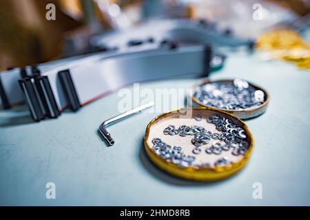 A lot of different metal bolts and nuts, plastic small components and professional tools lie on a blue desktop in a master worker's workshop under a c Stock Photo