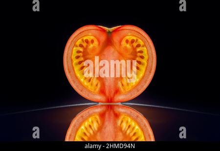 Slice of a tomato isolated in dark black background with reflection Stock Photo
