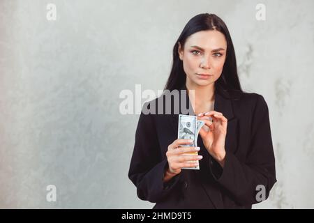 Young beautiful brunette woman in formal black suit holding dollar money wad. Passion and temptation concept Stock Photo
