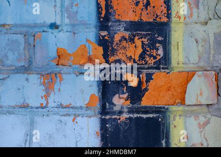 Old colorful orange blue black paint with cracks on red brick wall as background, texture, selective focus Stock Photo