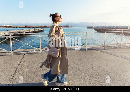 Young adult trendy stylish beautiful caucasian happy smiling woman enjoy walking by Yalta sea embankment on warm sunny day. Female person portrait Stock Photo