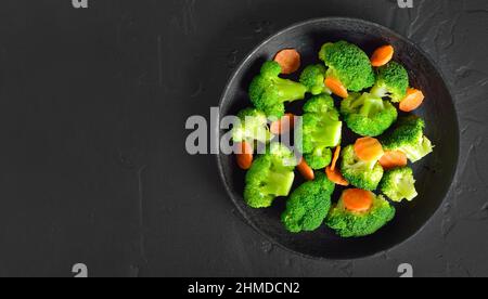 Broccoli and carrots in frying pan on black stone background with copy space.  Top view, flat lay Stock Photo