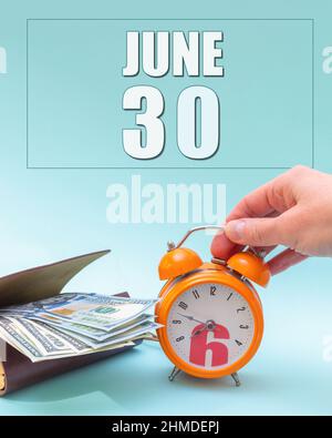 June 30th. Hand holding an orange alarm clock, a wallet with cash and a calendar date. Day 30 of month. Business planning. Time is money. Tax time. Su Stock Photo