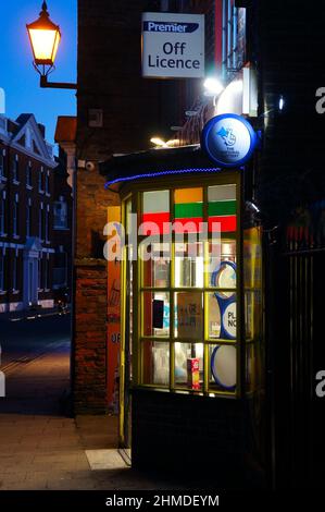 Old off licence shop with lit up bay window and street lantern at dusk Stock Photo