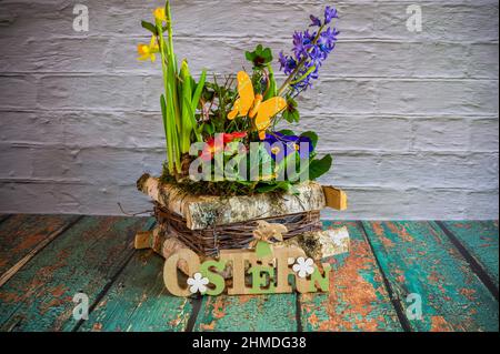 Flower arrangement with wooden sign as Easter decoration, the text on the sign is German for Easter. Stock Photo